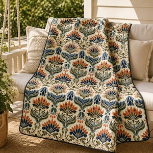 Peut inclure: Un jeté de lit matelassé orné d'un motif botanique répétitif avec des fleurs stylisées dans des tons orange brûlé, bleu profond et vert sauge sur un fond crème, fini avec un biais bleu foncé le long des bords du tissu.