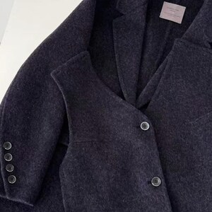 May include: A dark gray blazer and vest set. The blazer has a notched lapel, three buttons on the sleeve, and a two-button closure. The vest has a V-neck and three buttons. The fabric appears to be a soft wool blend.