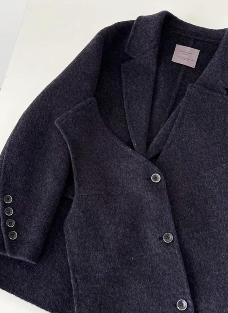 May include: A dark gray blazer and vest set. The blazer has a notched lapel, three buttons on the sleeve, and a two-button closure. The vest has a V-neck and three buttons. The fabric appears to be a soft wool blend.