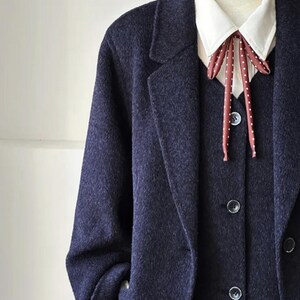 May include: A navy blue suit on a mannequin. The suit includes a long coat, vest, and a white collared shirt with a red and white polka dot bow tie. The suit has a classic, tailored design.