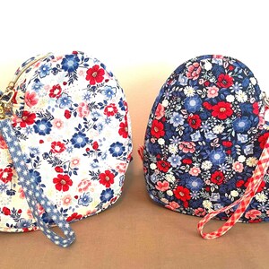 Puede incluir: Dos bolsos de tela con forma de coraz&oacute;n con estampados florales. Uno es blanco con flores rojas y azules, el otro es azul marino con flores rojas y rosas. Cada bolso tiene una correa de mu&ntilde;eca y una cremallera dorada.