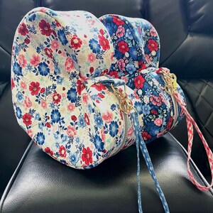 Puede incluir: Dos neceseres con estampado floral. Una bolsa tiene un fondo crema con flores rojas, rosas y azules. La otra bolsa tiene un fondo azul marino con flores rojas y rosas. Ambas bolsas tienen cremalleras doradas y correas de mu&ntilde;eca a juego.