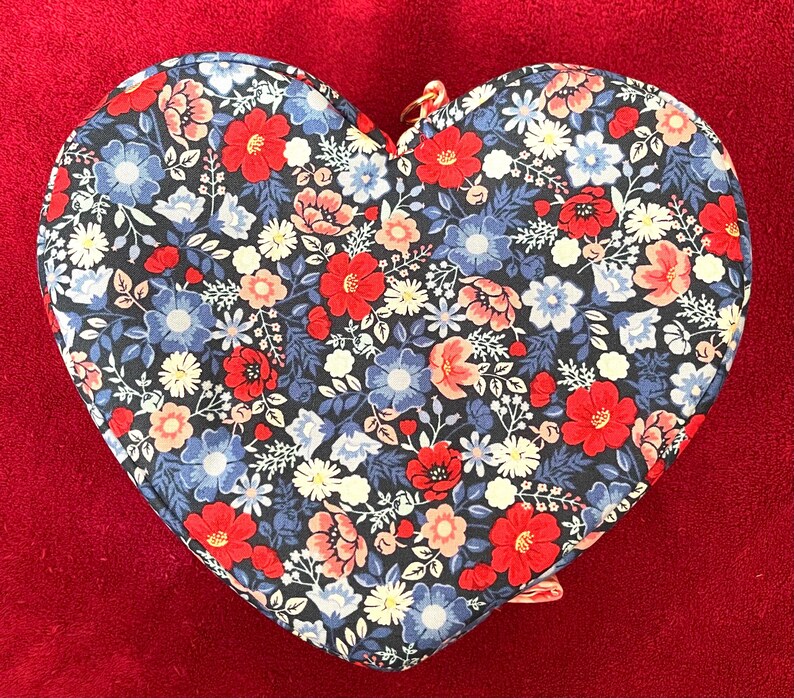 Puede incluir: Estuche para accesorios con estampado floral en forma de coraz&oacute;n. El estuche tiene un fondo oscuro con flores rojas, azules y blancas. Se ve una cremallera dorada.