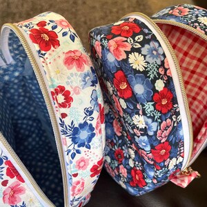 Puede incluir: Dos bolsas en forma de coraz&oacute;n abiertas, con estampados florales. Una bolsa tiene un fondo blanco con flores rojas, rosas y azules, y un interior de lunares azules. La otra tiene un fondo azul marino con flores rojas y rosas y un interior de cuadros vichy rojos y blancos.