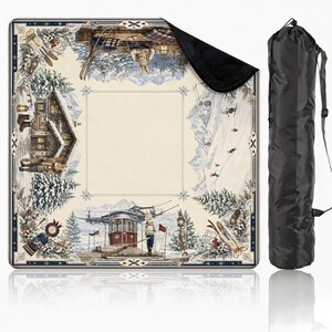 May include: A square outdoor blanket featuring a winter mountain scene with snow-covered chalets, skiers, and cable cars, with a cream-colored center and a black underside. The blanket is accompanied by a black cylindrical carrying bag with a strap.