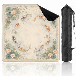 May include: A square outdoor blanket featuring a circular pattern of orange, white, and black koi fish swimming among water lilies and green lily pads on a light background, accompanied by a black cylindrical carrying bag with a shoulder strap.
