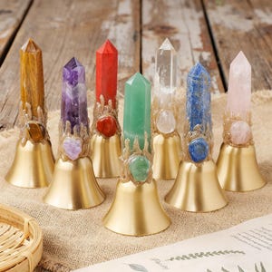 Può includere: Sette campane di cristallo di pietre preziose con basi color oro. I cristalli sono di vari colori, tra cui marrone, viola, rosso, verde, trasparente, blu e rosa. Ogni campana ha un accento decorativo color oro attorno al cristallo.