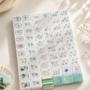 Könnte beinhalten: Ein Set aus weißen, rechteckigen Mahjong-Spielsteinen mit Illustrationen zum Thema Ozean, darunter Muscheln, Korallen, Meerestiere und nummerierte Reihen. Die Spielsteine zeigen blaue, grüne und violette Grafiken sowie einige Joker- und Buchstaben-Steine.