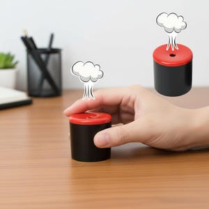 May include: A black and red cylindrical desk toy with a cartoon cloud graphic. The toy is held by a hand on a wooden desk. A second toy and a pencil holder are in the background.