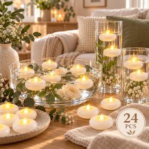 Può includere: Un set di 24 candele LED galleggianti bianche con luce gialla calda. Le candele sono esposte in ciotole e cilindri di vetro trasparente riempiti d'acqua, foglie di eucalipto verdi e fiori bianchi, con alcune candele su un piatto testurizzato.