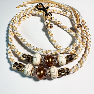 May include: Braided dog leash in white and gold. The leash features decorative beads in white, gold, and bronze. A gold-colored clasp and hardware complete the design. The leash is designed for pets.