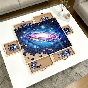 May include: A galaxy-themed jigsaw puzzle with a vibrant blue, purple, and white color scheme. The puzzle is partially assembled on a white table, with wooden trays holding puzzle pieces. The image shows a completed section of the puzzle.