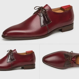 May include: A burgundy leather derby shoe featuring a smooth finish, dark brown laces, and a contrasting dark brown leather panel at the eyelets. The shoe includes a low stacked heel, a pointed toe, and a wooden shoe tree with a red heel insert.
