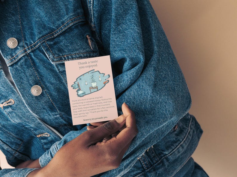 May include: A pink card with the text "Thank a taste you enjoyed" and a cartoon illustration of a blue creature with a cup. The card is held against a denim jacket.