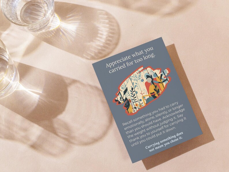 May include: A grey greeting card with the text "Appreciate what you carried for too long." The card features an illustration of plants and people. The card is on a light brown surface with two glasses.