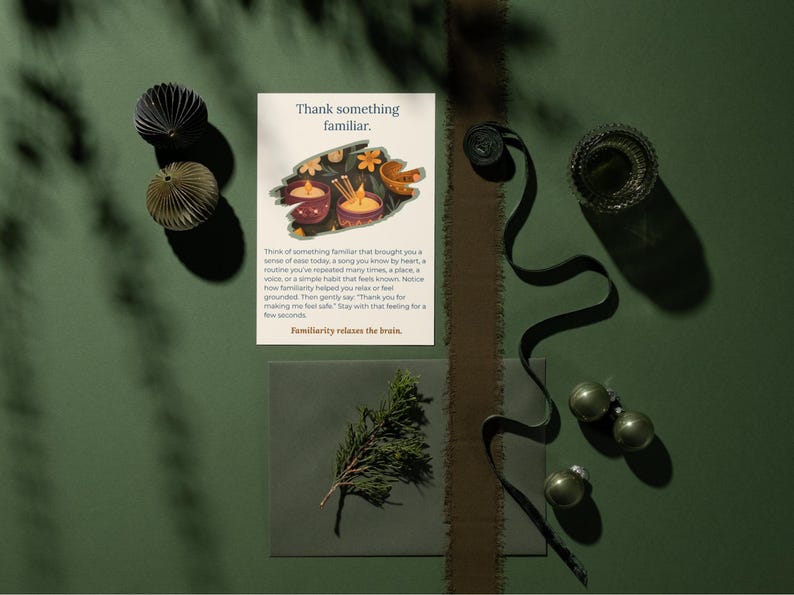 May include: An overhead shot features a greeting card with the text "Thank something familiar." Decorative paper ornaments, a sprig of greenery, and a dark ribbon are arranged on a green surface. The card's text is visible.