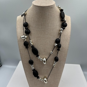 May include: A two-strand necklace with black and silver beads. The necklace features large, matte black beads interspersed with smaller silver beads and elongated silver beads. The necklace is displayed on a beige mannequin.