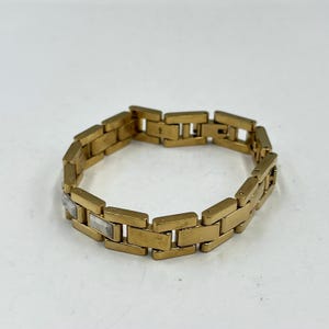May include: A gold-toned bracelet with rectangular links. The bracelet has a polished finish and features a few silver-colored rectangular accents. The bracelet is shown on a white background.
