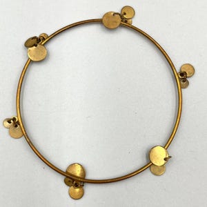 Può includere: Un braccialetto a cerchio color oro con piccoli ciondoli rotondi pendenti. Il braccialetto ha un design semplice e circolare con più ciondoli distribuiti uniformemente sulla circonferenza. I ciondoli sono anch'essi color oro e aggiungono un tocco di movimento.