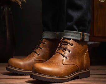 May include: Brown leather boots with laces. The boots have a textured appearance and a dark brown sole. The person is wearing dark blue jeans with the cuffs rolled up, revealing a lighter denim interior. The boots are on a wooden surface.