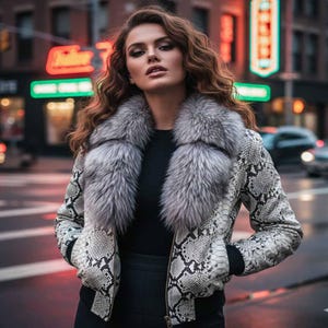 Pode incluir: Casaco elegante com padrão de pele de cobra em tons de cinza e branco, com uma gola luxuosa de pele cinza. Usado sobre um top preto, criando um contraste marcante. O fundo mostra uma cena de rua da cidade.