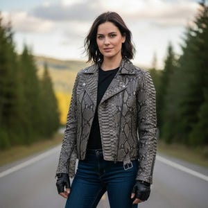 Peut inclure: Veste en cuir grise à motif peau de serpent, chemise noire et jean bleu. La veste de style motard a un col cranté, une fermeture éclair asymétrique et des détails à boutons-pression. La personne est sur une route.