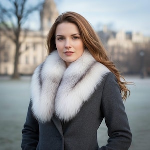 May include: A woman wearing a gray coat with a luxurious white and gray fur collar. The coat is buttoned up, and the background is blurred, suggesting an outdoor setting. The fur collar adds a touch of elegance to the outfit.