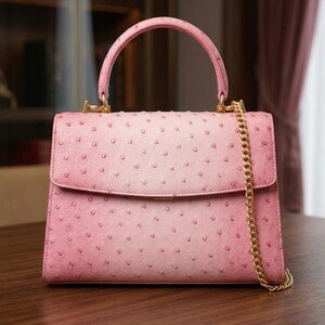 May include: A pink handbag with a top handle and a gold chain strap. The bag has a flap closure and a textured surface with small, evenly spaced dots. The hardware is gold-toned. The bag is sitting on a wooden surface.