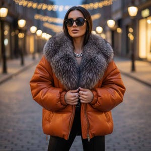 Puede incluir: Una chaqueta acolchada naranja con un gran cuello de piel gris. La chaqueta tiene cierre de cremallera y se usa sobre una parte superior oscura. El fondo muestra una calle de la ciudad con luces borrosas.