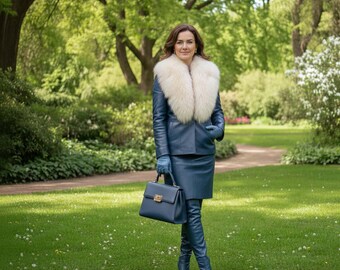 May include: A woman in a blue leather jacket with a white fur collar, matching skirt, gloves, and knee-high boots, holding a blue handbag. The background is a green park with trees and grass.