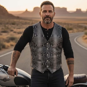 May include: A grey snakeskin-patterned waistcoat with a button-up front. The waistcoat is worn over a black long-sleeved shirt and paired with black jeans. The person is standing next to a motorcycle on a desert road.