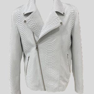Peut inclure: Veste en cuir blanc texturé avec un motif peau de serpent. La veste présente une fermeture éclair asymétrique, des revers crantés et des détails argentés. Un style motard classique avec une esthétique moderne et audacieuse.