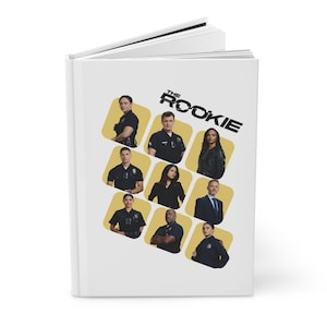 Könnte beinhalten: Ein weißes Notizbuch mit dem Titel "THE ROOKIE" in Schwarz. Das Cover zeigt Bilder der Darsteller in gelben und schwarzen Quadraten. Das Notizbuch ist geöffnet und zeigt leere Seiten.