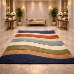 May include: A large, colorful area rug with a wavy striped design. The rug features bands of navy blue, rust, tan, light blue, cream, olive green, and burnt orange. The rug is placed in a luxurious room with a chandelier and a sofa.