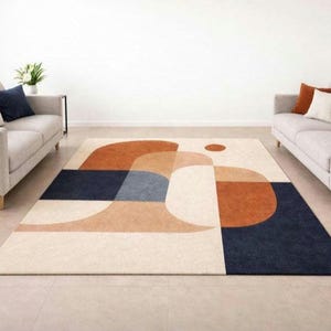 May include: A rectangular area rug with a geometric design in cream, navy blue, rust, and light blue. The rug is placed between two light gray sofas with accent pillows. The room has a minimalist aesthetic.