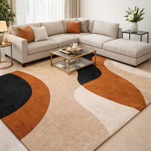May include: A modern living room rug with an abstract design. The rug features a beige background with large, curved shapes in black, burnt orange, and cream. The rug is placed in front of a beige sectional sofa with orange and cream throw pillows.