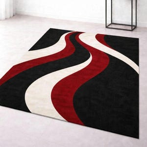 May include: A rectangular area rug with a bold, modern design. The rug features a black background with flowing, wavy stripes of red and off-white. The rug is placed on a light-colored tile floor.