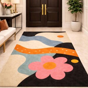 May include: A colorful area rug with a large pink flower design, orange and blue wave-like shapes, and a black border. The rug is rectangular and placed in a hallway with a dark brown door.