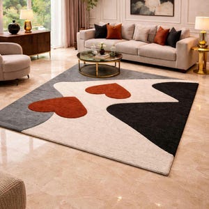May include: A modern area rug with a geometric design in gray, black, white, and rust-orange. The rug features two rust-orange heart shapes and a zig-zag pattern. The rug is placed on a polished marble floor in a living room setting.