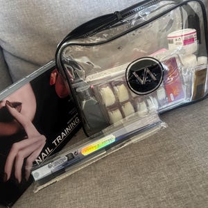 May include: A transparent cosmetic bag with a black zip, containing nail supplies, next to a box marked "NAIL TRAINING." The bag holds nail tips, bottles, and a jar. A nail art pen is also visible.