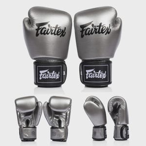 May include: A pair of silver boxing gloves with the brand name "Fairtex" printed in black on the gloves and wrist straps. The gloves are displayed in multiple angles, showcasing their design and features.
