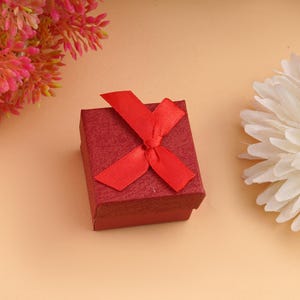 Red gift box with a bow on a peach backdrop, with pink and white flowers nearby—perfect gift for her 925 silver ring.