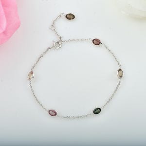 Puede incluir: Una delicada pulsera de plata con piedras preciosas ovaladas en varios colores, incluyendo marrón, rosa y verde. La pulsera tiene un diseño de cadena con cierre de broche. Las piedras están espaciadas uniformemente.
