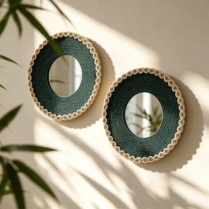 May include: Two circular wall mirrors featuring dark green rope-wrapped frames. Each mirror is bordered by a decorative, light beige braided trim that encircles the outer edge, creating a textured, layered appearance around the reflective glass centre.