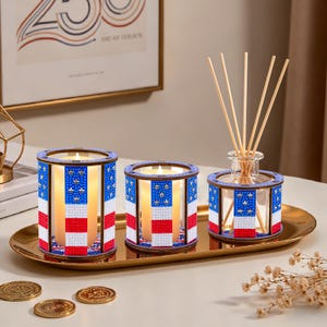 May include: A decorative set featuring two candle holders and a reed diffuser, all adorned with a patriotic red, white, and blue design. The candle holders and diffuser are arranged on a gold-colored tray, creating a cohesive home decor ensemble.