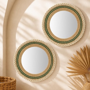 Puede incluir: Dos espejos de pared circulares con marcos envueltos en cuerda de yute de color tostado natural, acentuados con anillos concéntricos de cordón verde oscuro y terminados con un borde decorativo de cuerda blanca festoneada en el exterior.
