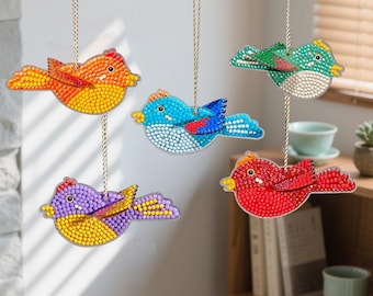 May include: Five beaded bird ornaments in various colors, including orange, blue, green, red, and purple. Each bird is suspended by a gold string. The birds have detailed beadwork and are designed to hang as decorations.