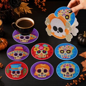 Puede incluir: Un juego de posavasos redondos con diseños de calaveras en diamond painting, que incluye un soporte con forma de calavera. Cada posavasos muestra un motivo único de calavera de azúcar con colores vibrantes, decorado con pedrería.