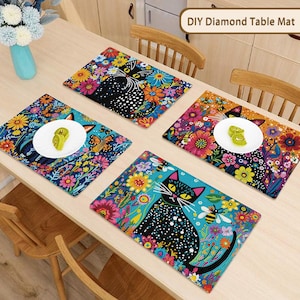 May include: Four colorful DIY diamond table mats with floral and cat designs. Each mat features a black cat with white polka dots, surrounded by vibrant flowers and butterflies. The mats are on a light wood table.