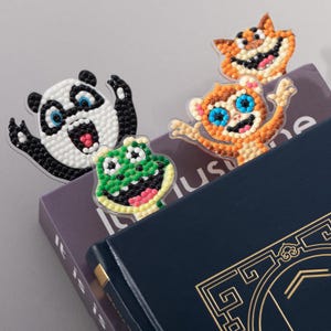 May include: Four animal-shaped bookmarks featuring a panda, a frog, a monkey, and a cat. Each bookmark is crafted with a beaded, mosaic-style surface on a clear acrylic base, displaying vibrant colors and expressive faces for each character.